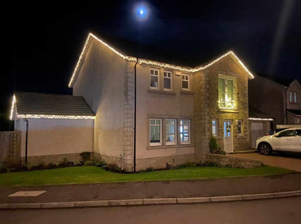 Warm white Christmas lights installed along the roofline of a house in Fife